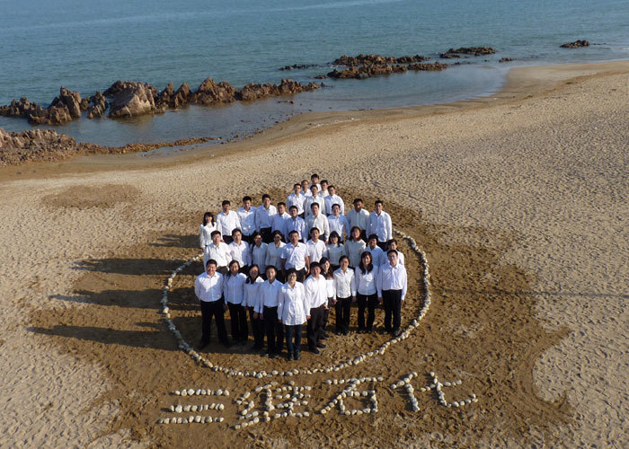 员工在沙滩上用身体和鹅卵石组成三维工程的logo造型，体现出员工对公司的热爱